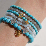 A stack of gemstone bracelets including the Inner Voice Lotus Gemstone Bracelet, showcasing vibrant turquoise and various charms. Ideal for yoga and spiritual practice, these malas serve as talismans for protection and meaningful self-expression.