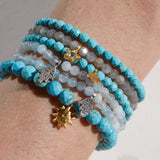 A stack of gemstone bracelets including the Inner Voice Lotus Gemstone Bracelet, showcasing vibrant turquoise and various charms. Ideal for yoga and spiritual practice, these malas serve as talismans for protection and meaningful self-expression.